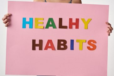 A woman holds a pink poster with colorful letters spelling 'HEALTHY HABITS'.
