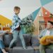 Mother, father and adorable active kid are fighting pillows having fun together on sofa in house enjoying family activity. People, happiness and youth concept.